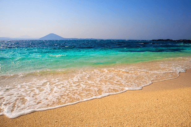 모래 사장이 있고 청록색의 바다가 잔잔하게 있는 제주 바다 풍경이다. 멀리 작은 섬이 보인다.