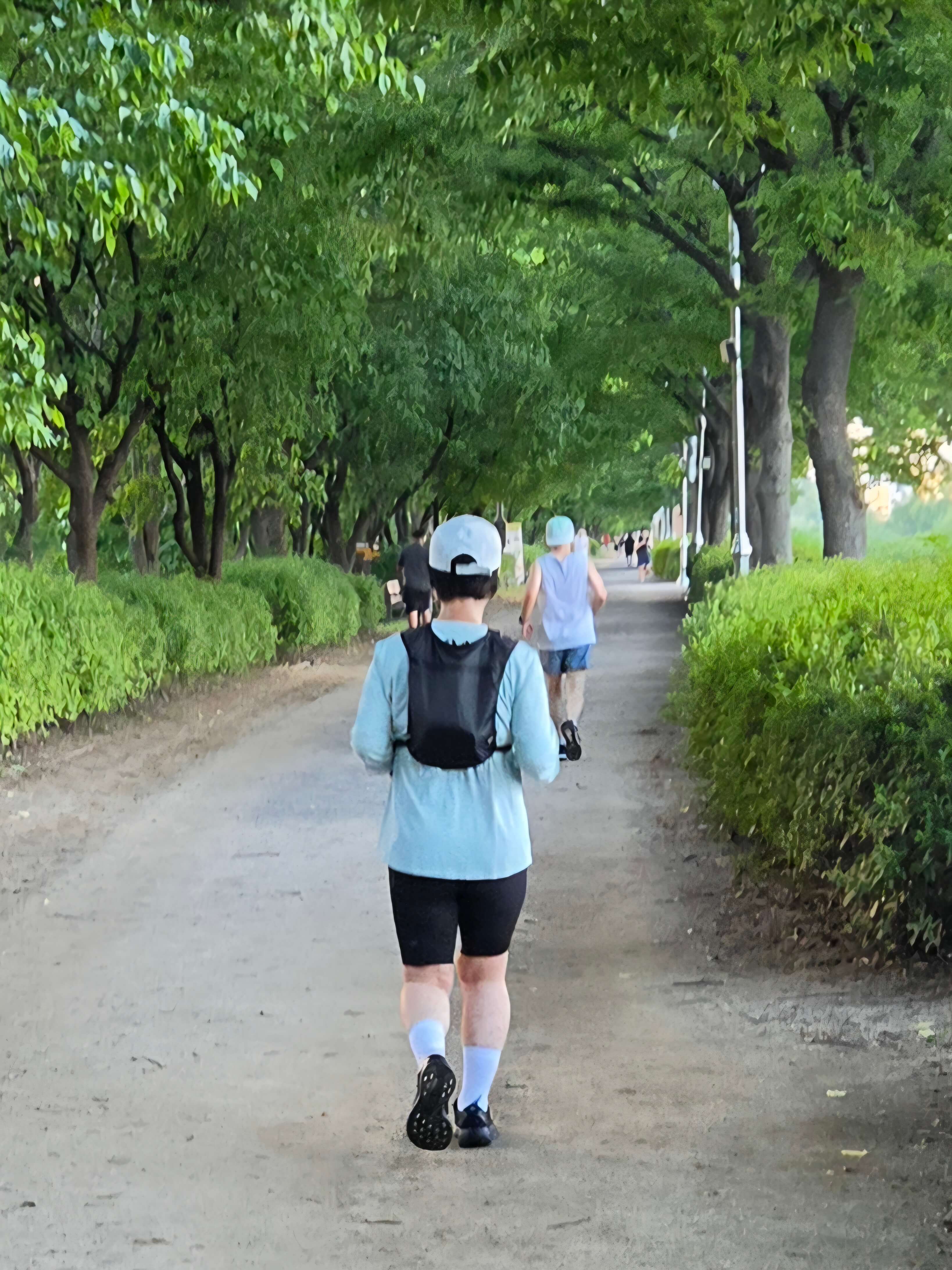 가로수가 우거진 산책로에서 러닝 베스트를 착용하고 야외 러닝을 즐기는 뒷모습