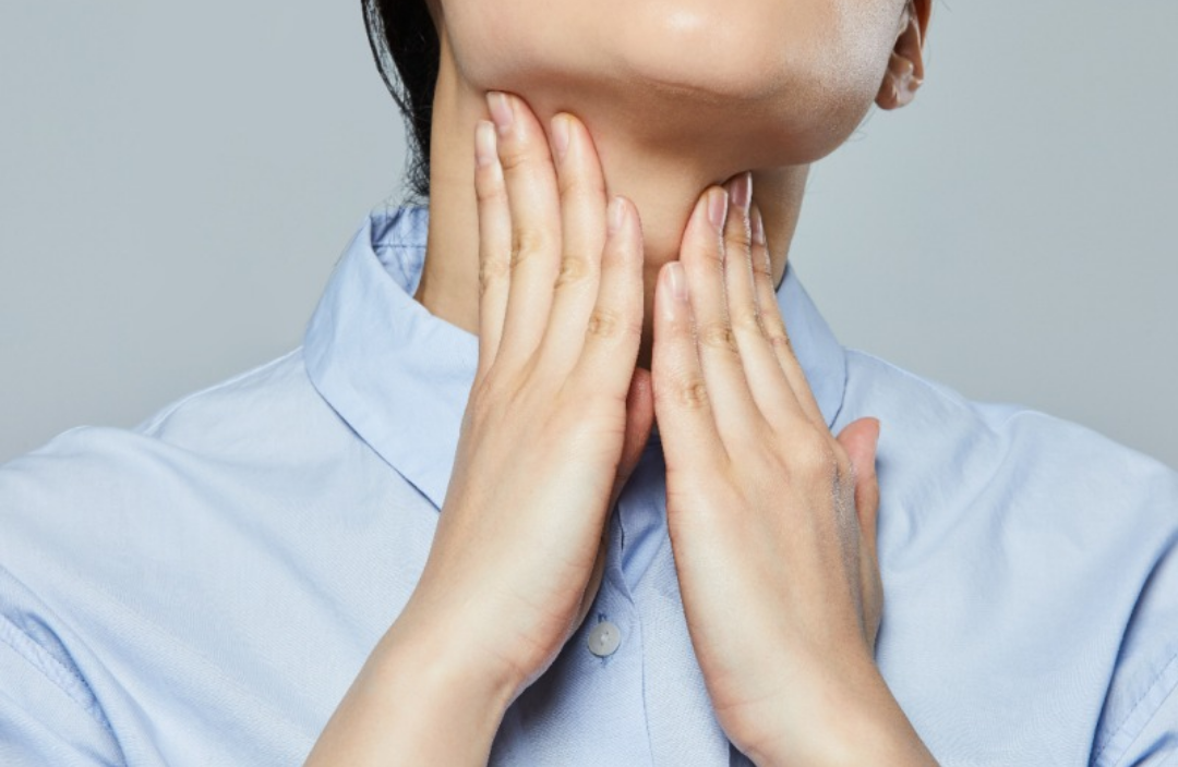 한 여자가 두 손으로 목을 만지며 괴로워하고 있다.