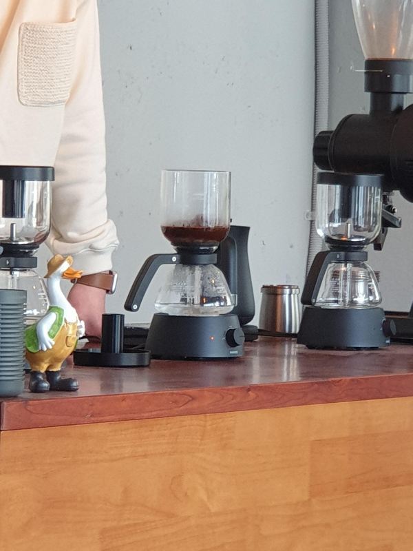 테이블 위 사이폰 추출 도구에 커피가 추출되는 모습. 하부 플라스크에는 물, 상부에는 추출 중인 커피가 보인다.