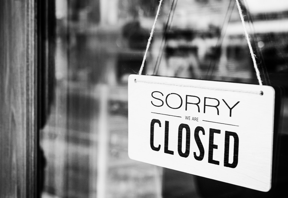 유리창에 걸린 'SORRY WE ARE CLOSED' 문구의 나무 팻말과 폐업한 가게의 모습