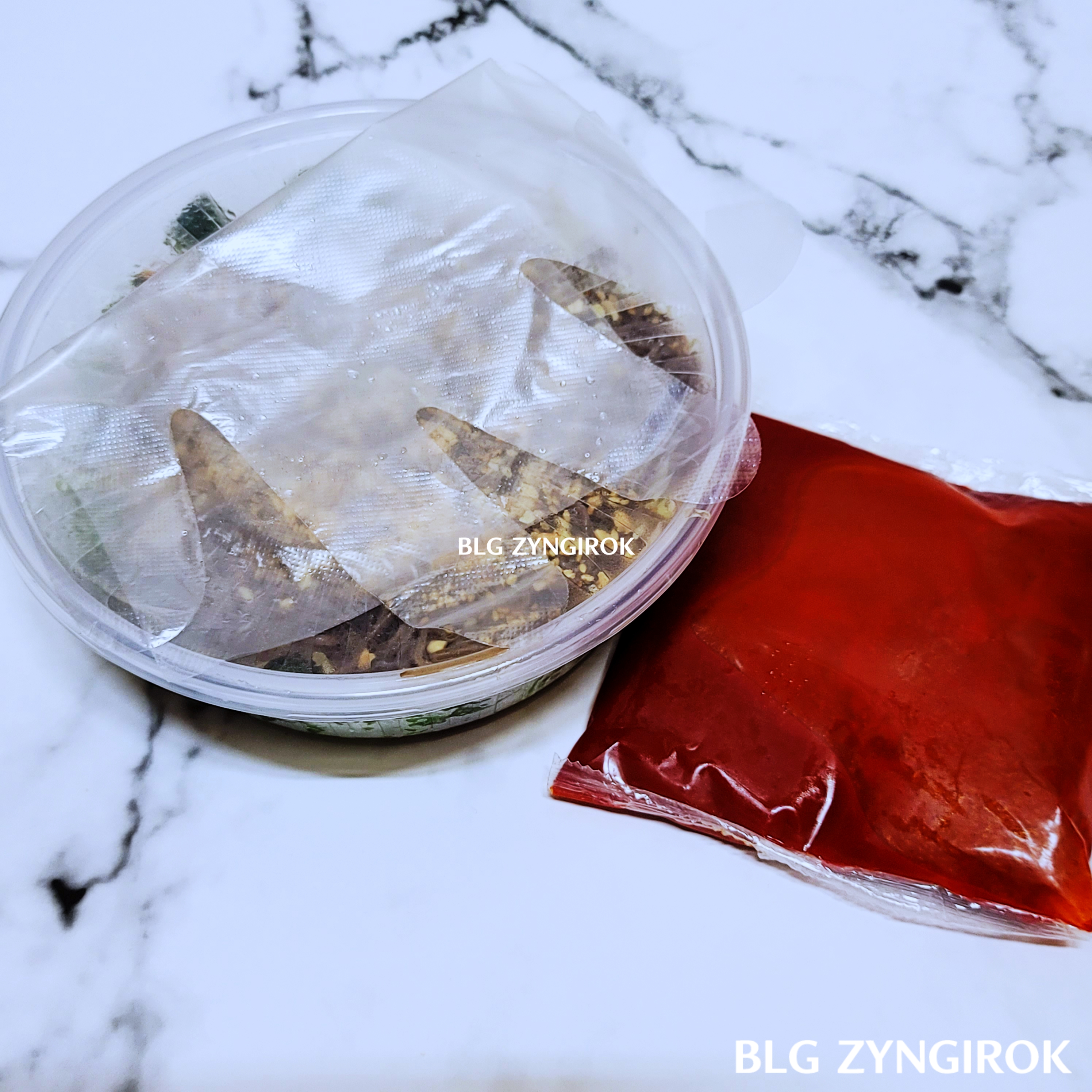 막국수-구성품-모습이다.-플라스틱-통에담겨있는-막국수.-그-통위에-위생장갑이-하나-놓여있다.-막국수-오른편에는-빨간색-소스가-비닐포장되어-놓여있다.