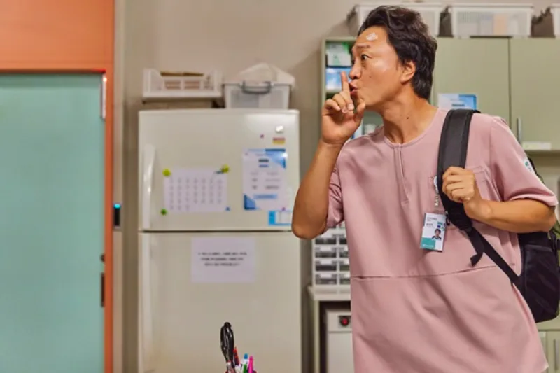 탕비실을 배경으로 분홍색 상의에 검은 가방을 메고 있는 드라마 정신병동에도 아침이 와요의 윤만천 캐릭터