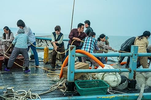 부두에서 여러 명의 어부들이 함께 밧줄을 당기며 고기잡이 작업을 하고 있는 장면