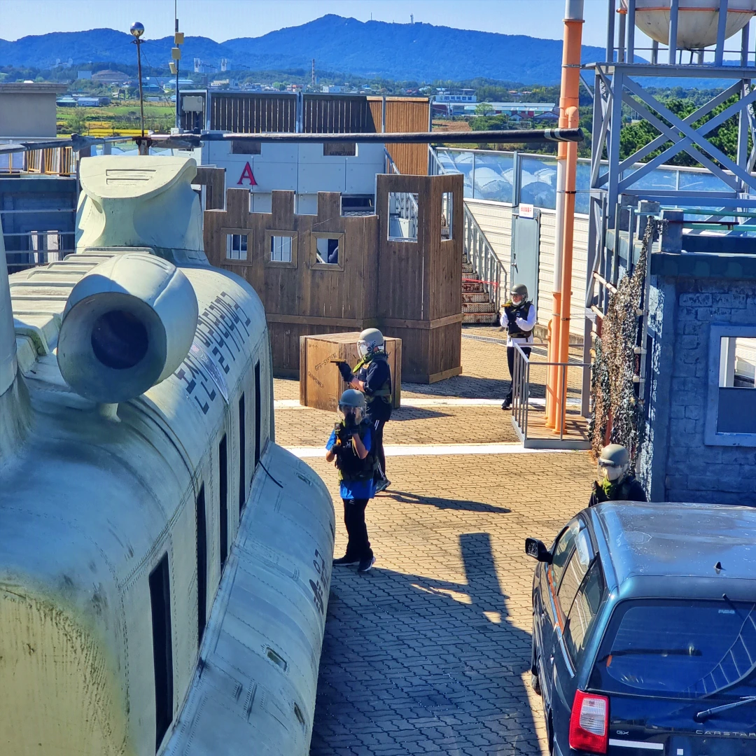 차와 건물이 있는 거리에서 보호복을 입은 3사람이 총을들고 주위를 경계하고 있다