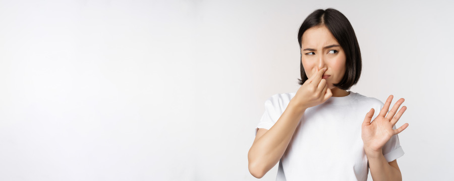 하얀색 티셔츠를 입은 젊은 여성이 방귀 냄새 때문에 손으로 본인의 코를 잡고 냄새를 억제하고 있는 것을 찍은 사진