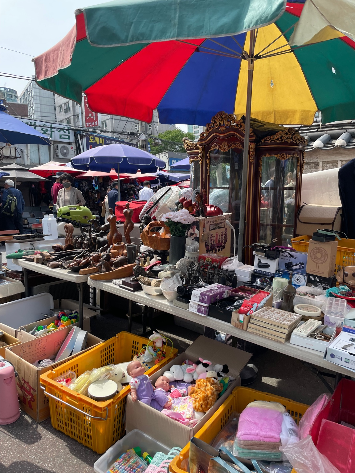 "Flea market scene at Dongmyo, Seoul, with secondhand electronics, toys, and vintage goods displayed under colorful umbrellas."