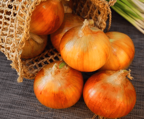 갈색 망 가방에서 갈색 껍질이 있는 양파들이 쏟아져 나오는 장면이다. 양파는 크고 동그랗게 생겼다.