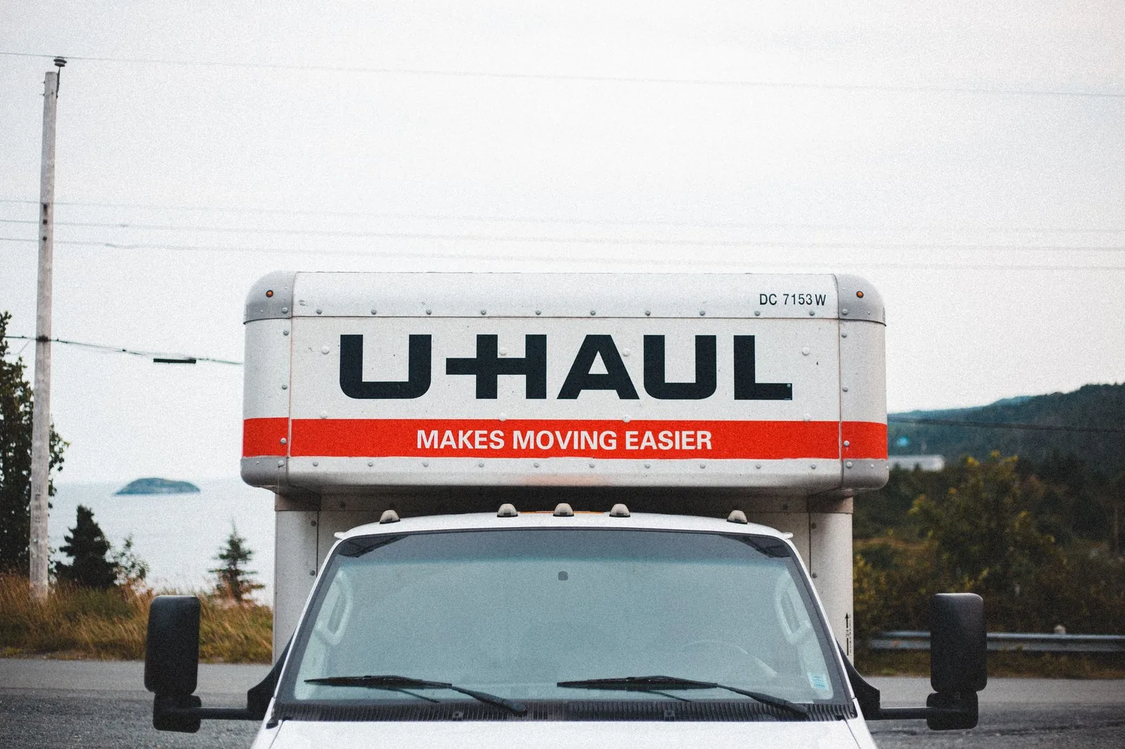 경치 좋은 야외 배경에 의해 도로 옆에 주차된 U-Haul 이사 트럭.