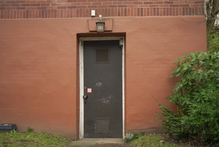 붉은 벽돌 건물 외벽에 설치된 어두운 철문, 전세사기로 인해 거주지를 잃은 피해자의 불안정한 주거 현실을 상징하는 이미지