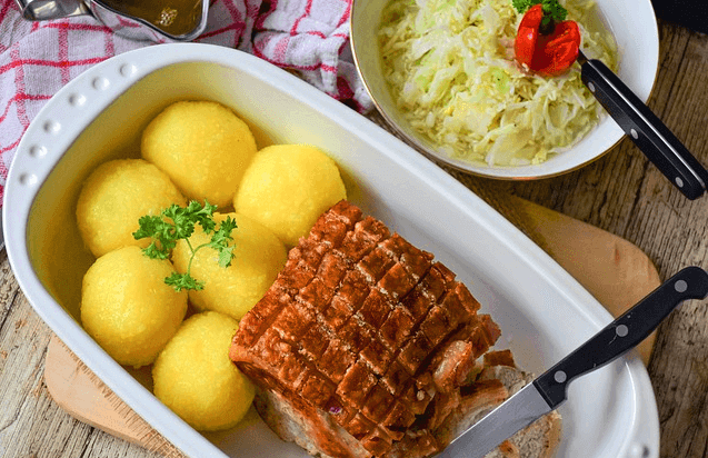 기다란 플라스틱 그릇에 돼지껍데기 구이가 있고, 잘 익은 노란 감자 6개가 있다.