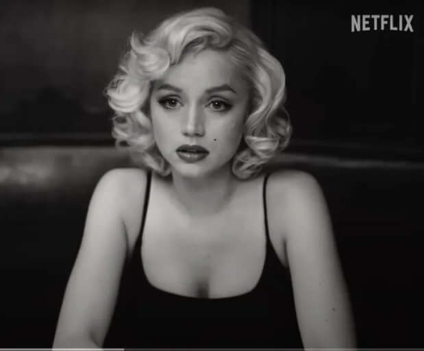 Blonde : 마릴린 먼로가 어두운 배경 속에서 정면을 응시하고 있으며, 감정이 섞인 표정으로 앉아 있는 모습