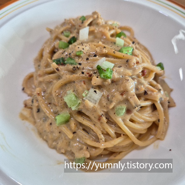 A finished plate of Doenjang pasta topped with chopped green onions and black pepper