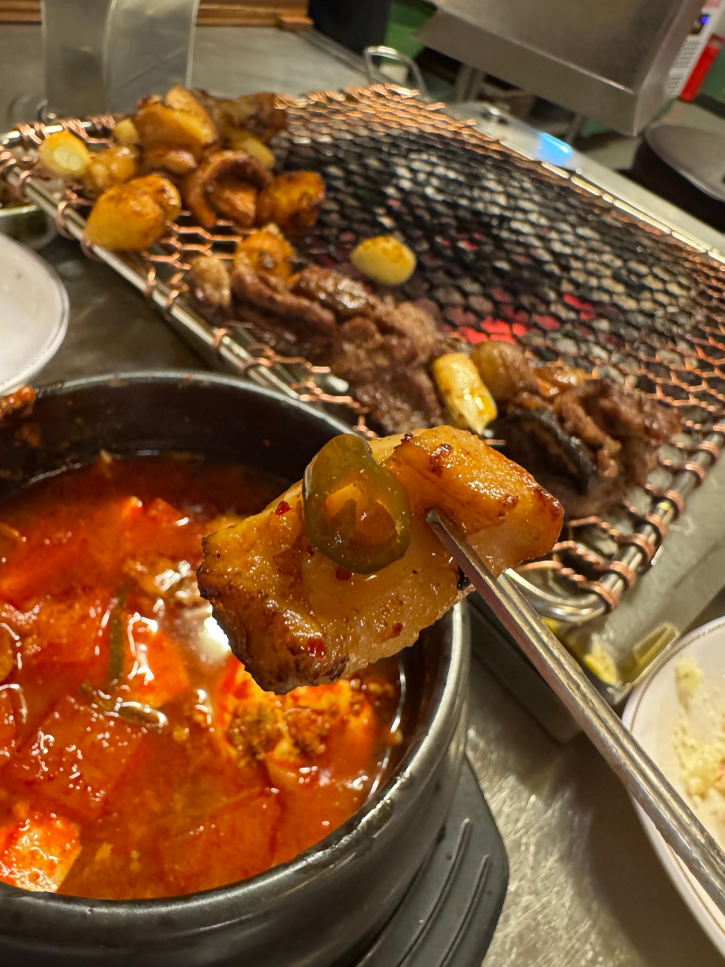 세광양대창 정자점 불판 위에서 노릇하게 구워진 대창을 고추장아찌와 함께 젓가락으로 들어 올리는 장면&amp;#44; 바삭한 겉면과 윤기 흐르는 속살이 대비되어 식욕을 자극하는 모습