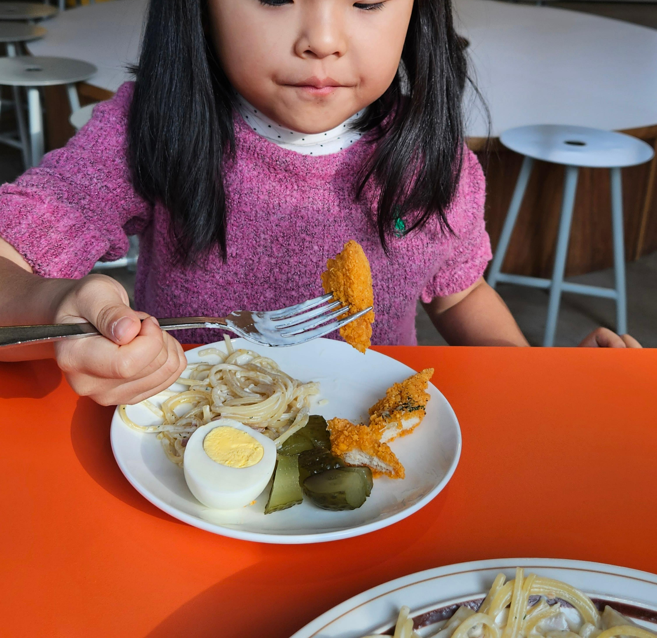 핑크색 옷을 입은 아이가 포크로 돈가스를 집어 맛있게 먹고 있는 모습