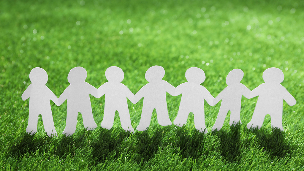 푸른 잔디밭에서 서로 손을 잡고 서 있는 종이 인형들