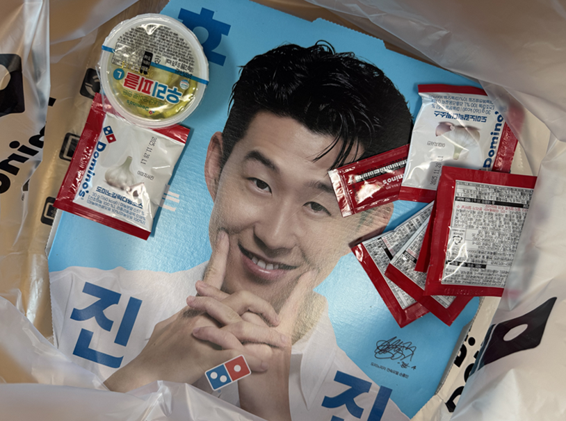 도미노피자 포장 주문 구성품&amp;#44; 손흥민 포스터와 각종 소스 포함된 포장 이미지