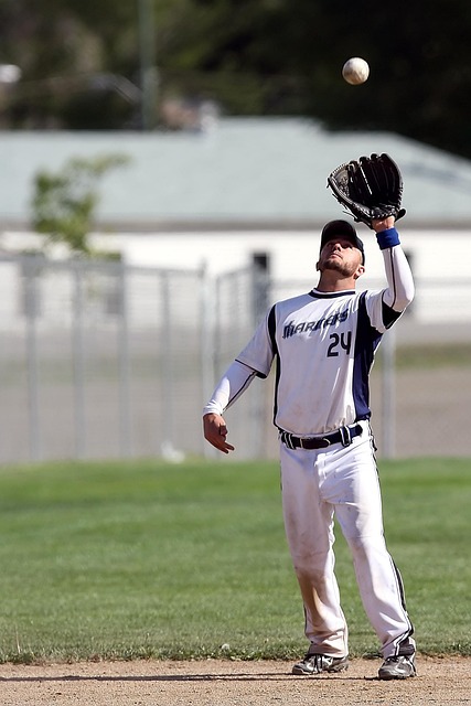 흰색 유니폼의 야구 선수가 글러브를 끼고 뜬공을 잡기 위해 위를 바라보며 점프하고 있는 모습.