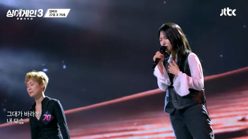 싱어게인3- 무대 왼쪽 검정색 롱원피스에 갈색 숏컷을 하고 앞을 바라보며 서있는 58호와 청바지에 흰셔츠 검정색 조끼를 입고 웨이브진 긴머리로 오른손에 마이크를 잡고 서서노래하는 27호