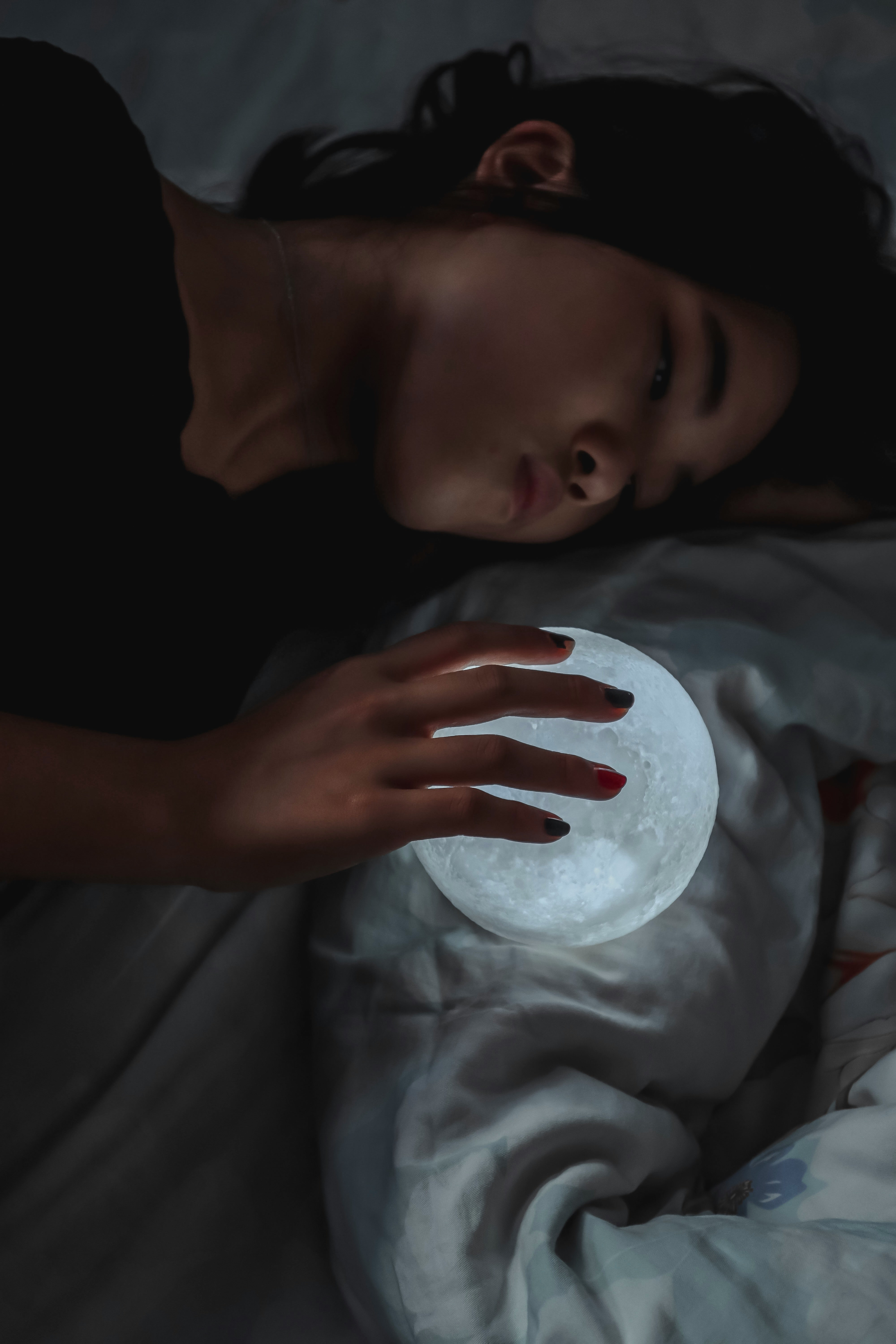 침대에서 옆으로 누워 손을 올린 달모양 조명을 바라보는 여자