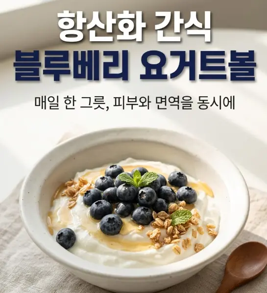 흰 도자기 볼에 담긴 그릭 요거트 위로 블루베리, 그래놀라, 꿀을 올린 요거트볼. 나무 스푼과 린넨 천 위에 자연광으로 촬영한 건강 간식 스타일링