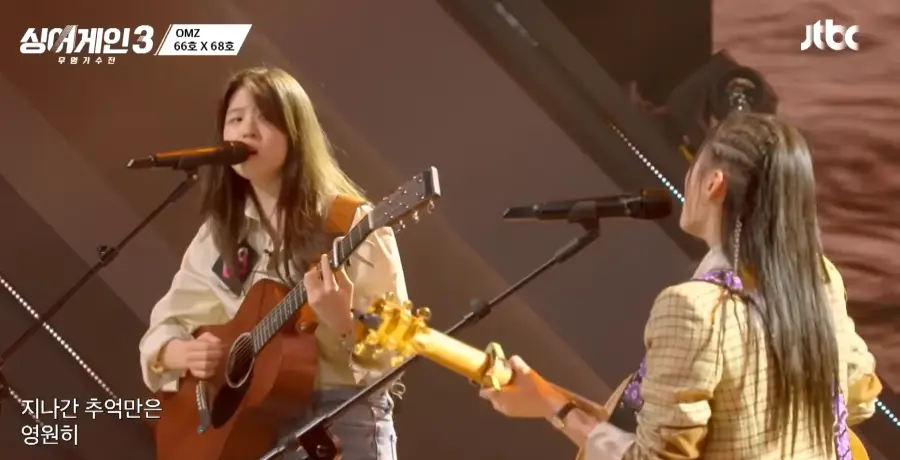 싱어게인3-
좌측 흰셔츠 청바지를 입고 갈색기타를 치며 긴생머리를 늘어뜨린채 스탠딩마이크 앞에서 66호를 보며 노래하는 68호와 우측 베이지색 자켓을 입고 연갈색 기타를 치며 긴생머리를 늘어뜨린채 스탠딩마이크에 입을 대고 노래하는 66호의 뒷모습