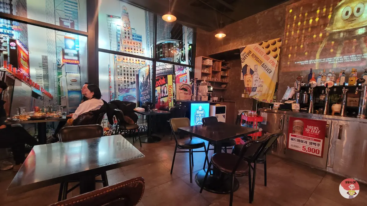 피맥 하우스 내부로, 벽화와 광고판이 있고, 손님들이 앉아 있으며, 바에는 맥주와 주류가 진열되어 있다