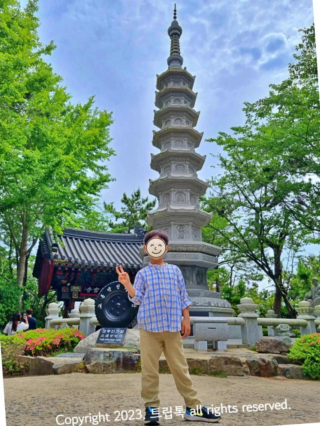 교통안전돌탑이 있고 그 아래 검정 타이어가 있다. 그 앞에 한 아이가 서 있다.