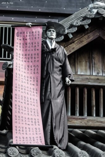 저스사자가-지붕위에서-살생부-명부가-적힌-족자를-펼치고-있는-모습