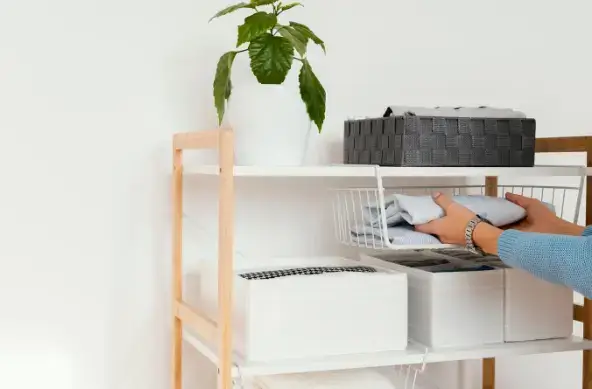 정리정돈을 위해 선반 위 바구니에 옷을 정리하고 있는 모습과 다양한 수납박스가 놓인 살림 공간 이미지