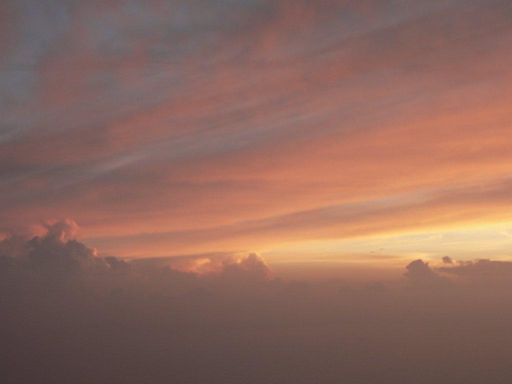하늘을 붉게 물들인 저녁노을. 부드럽게 퍼지는 주황빛과 분홍빛 구름이 수평선 위로 펼쳐져 있으며, 아래쪽에는 어두운 구름이 실루엣처럼 자리잡고 있다. 평온하고 몽환적인 분위기를 자아내는 일몰 장면이다.