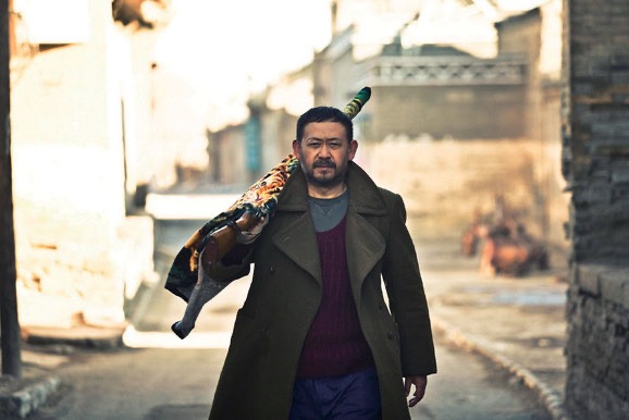 영화 《천주정》에서 주인공이 낡은 마을 골목을 걸으며 인형을 어깨에 메고 가는 장면. 한 사람의 인생을 짊어진 듯한 무거운 걸음은 상실과 용서, 그리고 세월의 깊이를 말없이 전달한다.