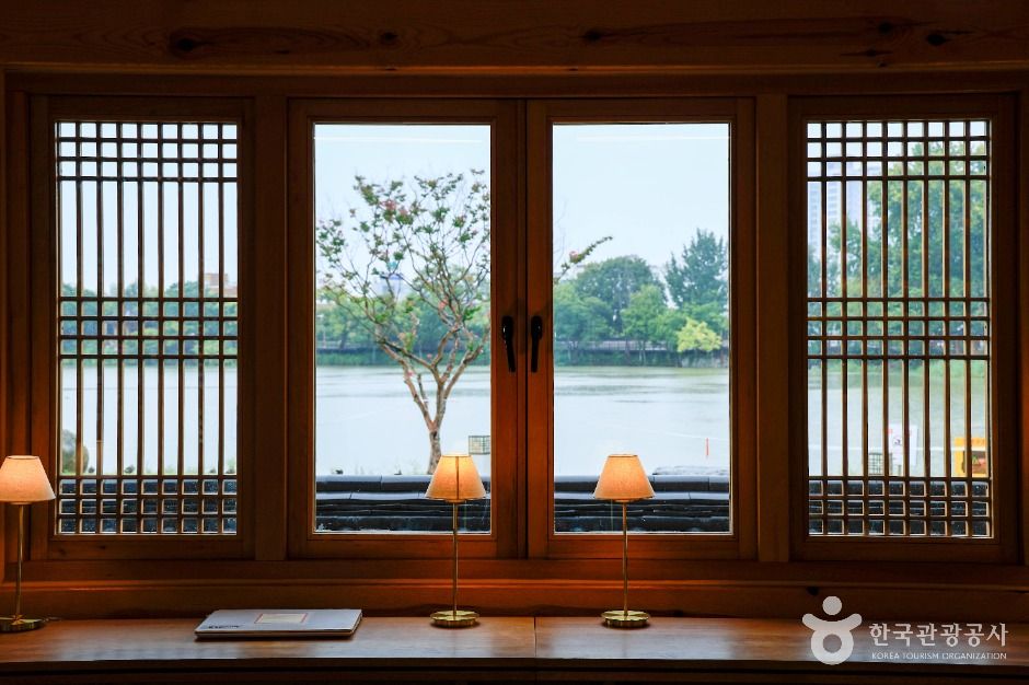 연화정도서관 내부의 따뜻한 우드톤 인테리어와 창밖으로 보이는 덕진공원 호수 뷰