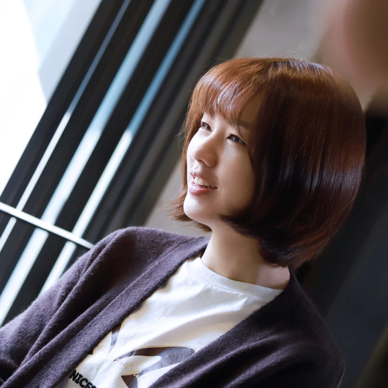 어느 실내 창가 옆에 갈색 단발머리를 하고 보라색 가디건을 입고 웃고 있는 안은진