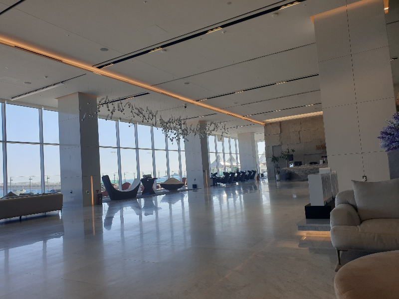 로비 전면에 바다가 보이는 유리창이 있다. 그 앞으로 소파들이 배치되어 있다.