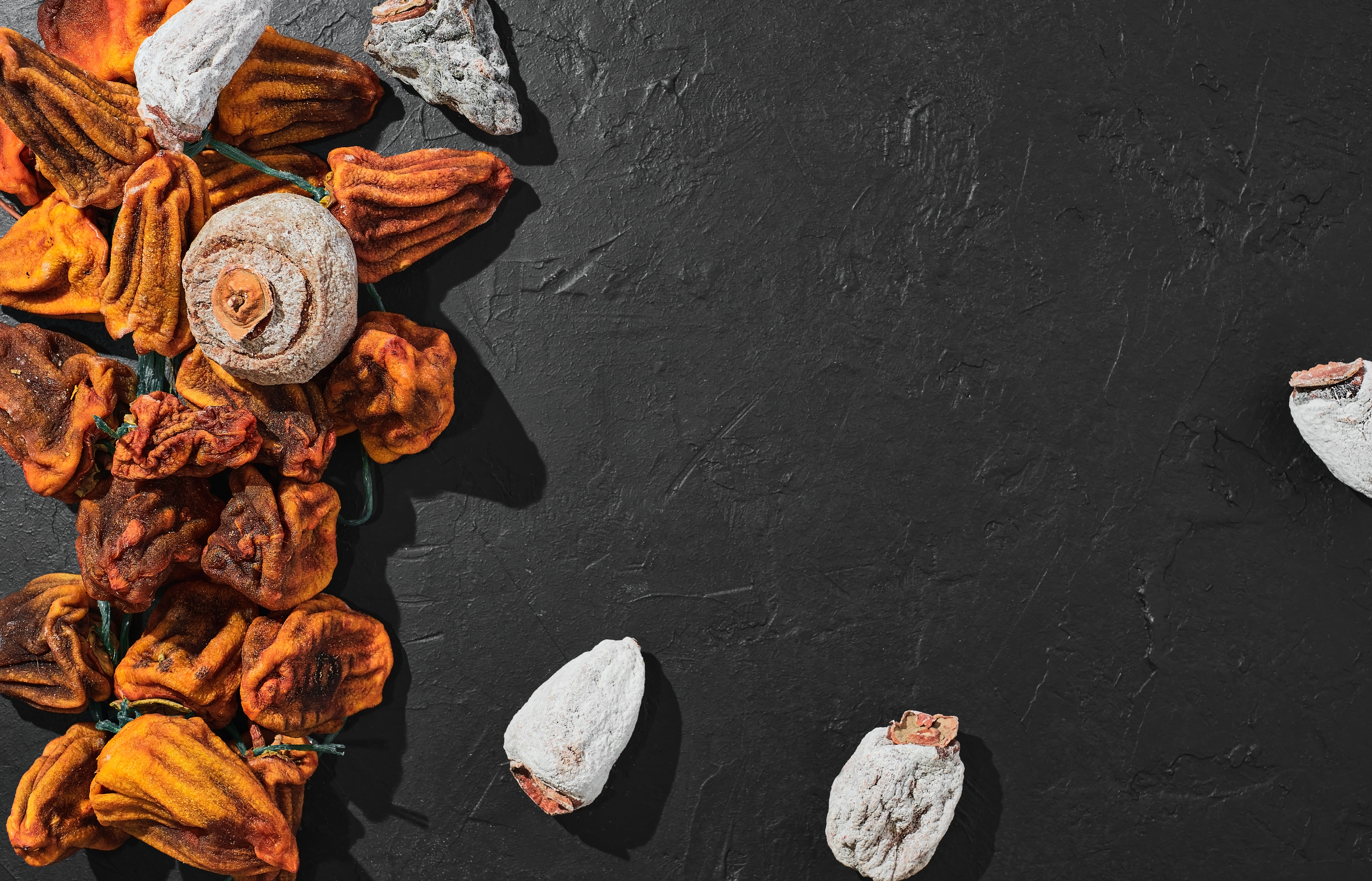 검은 바닥 위에 하얗게 분이 오른 곶감과 그렇지 않은 곶감이 어우러져 있는 사진 - 태양인(太陽人)에게 맞는 음식