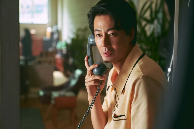 어느 실내를 배경으로 유선전화기를 들고 통화하고 있는 영화 밀수의 배우 조인성