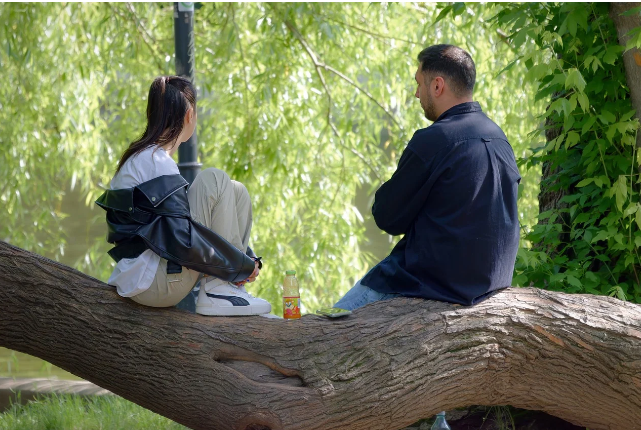 공원에서 나무에 앉아 조용히 대화 중인 두 사람, 진지한 분위기의 남녀