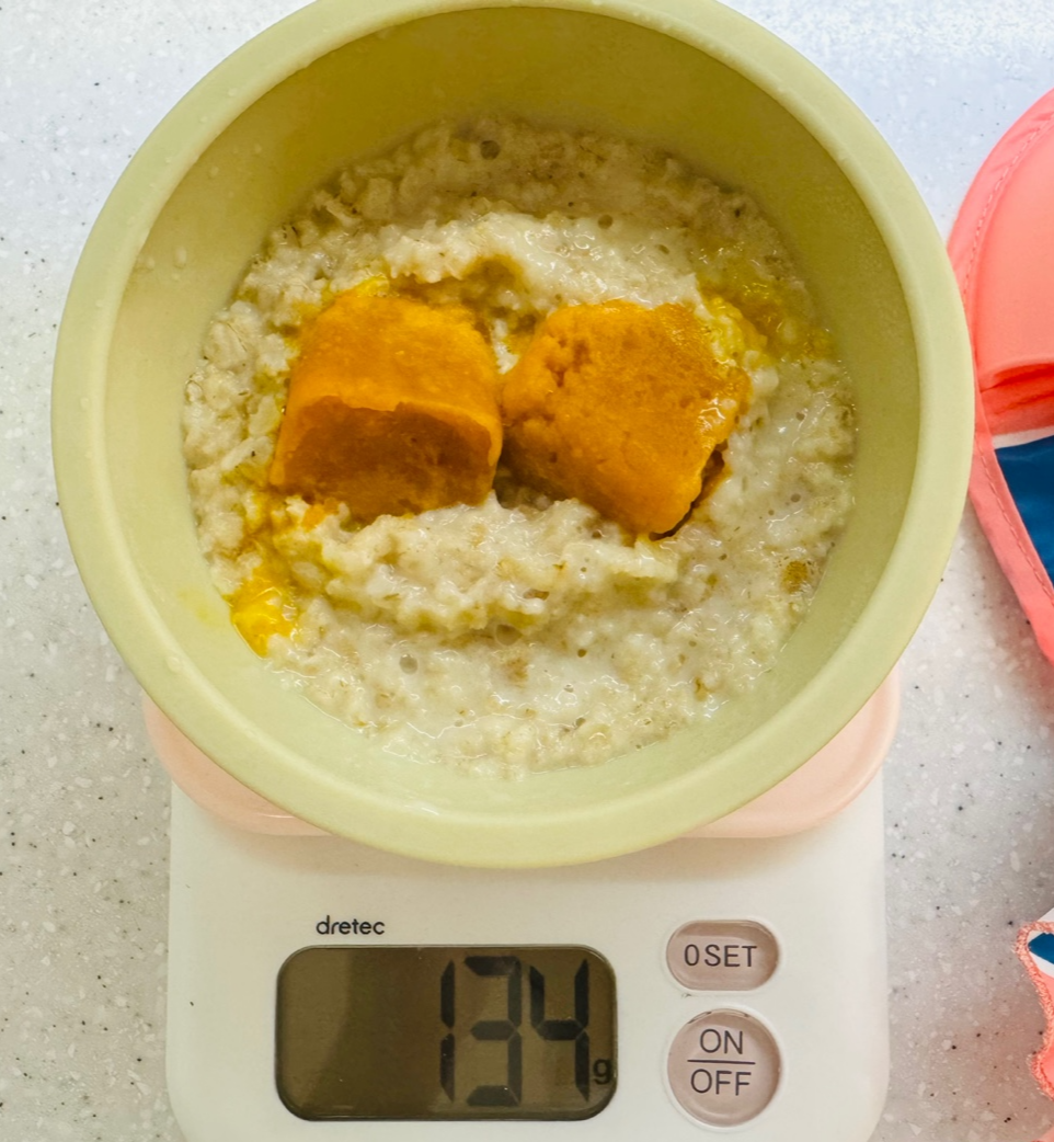 주방 저울 위에 단호박 큐브 2개가 올라간 오트밀포리지를 담은 아기용 이유식 그릇