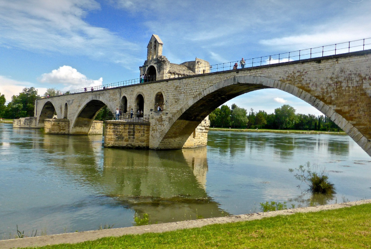 파란 하늘 아래 강이 있고, 벽돌로 구성된 다리가 강을 가로지르고 있으며 사람들이 다리를 건너고 있다.(아비뇽)