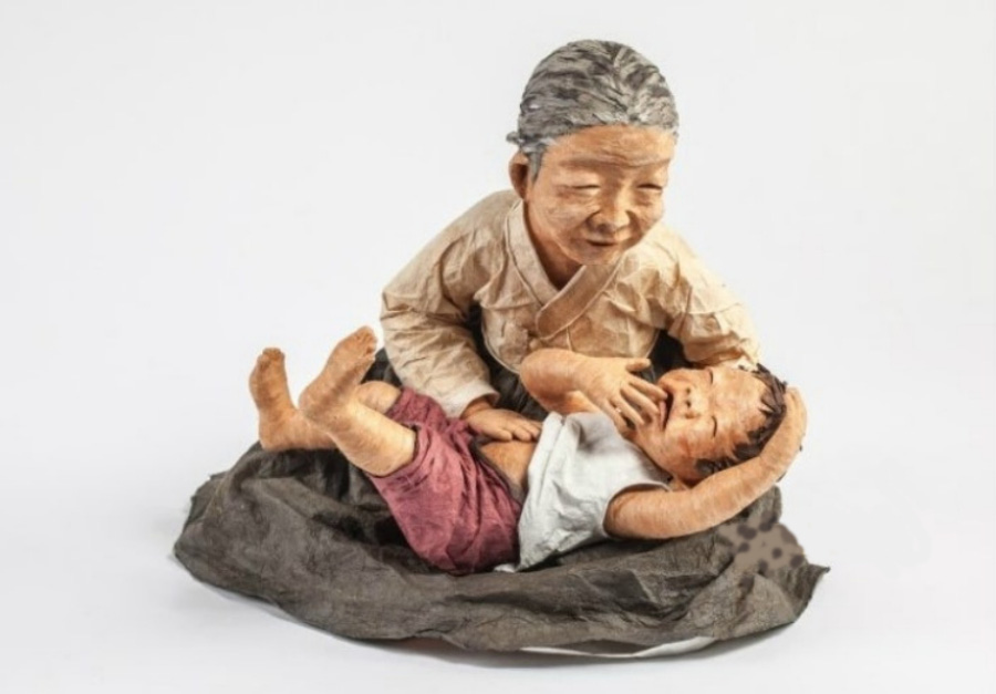 손자가 배가 아프다고 해서, 할머니가 손자를 무릎에 눕히고 손으로 배를 쓰다듬고 있는 것을 닥종이 공예로 형상화한 이미지 사진