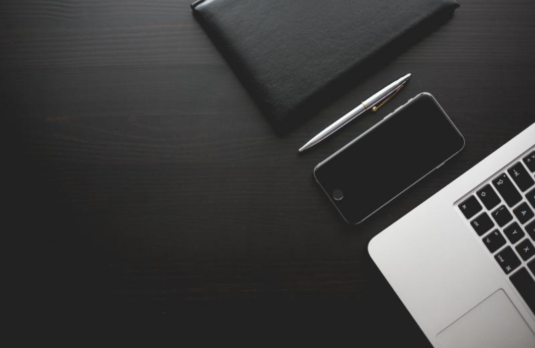 검은책상에 노트와 핸드폰 노트북이 놓여있다.