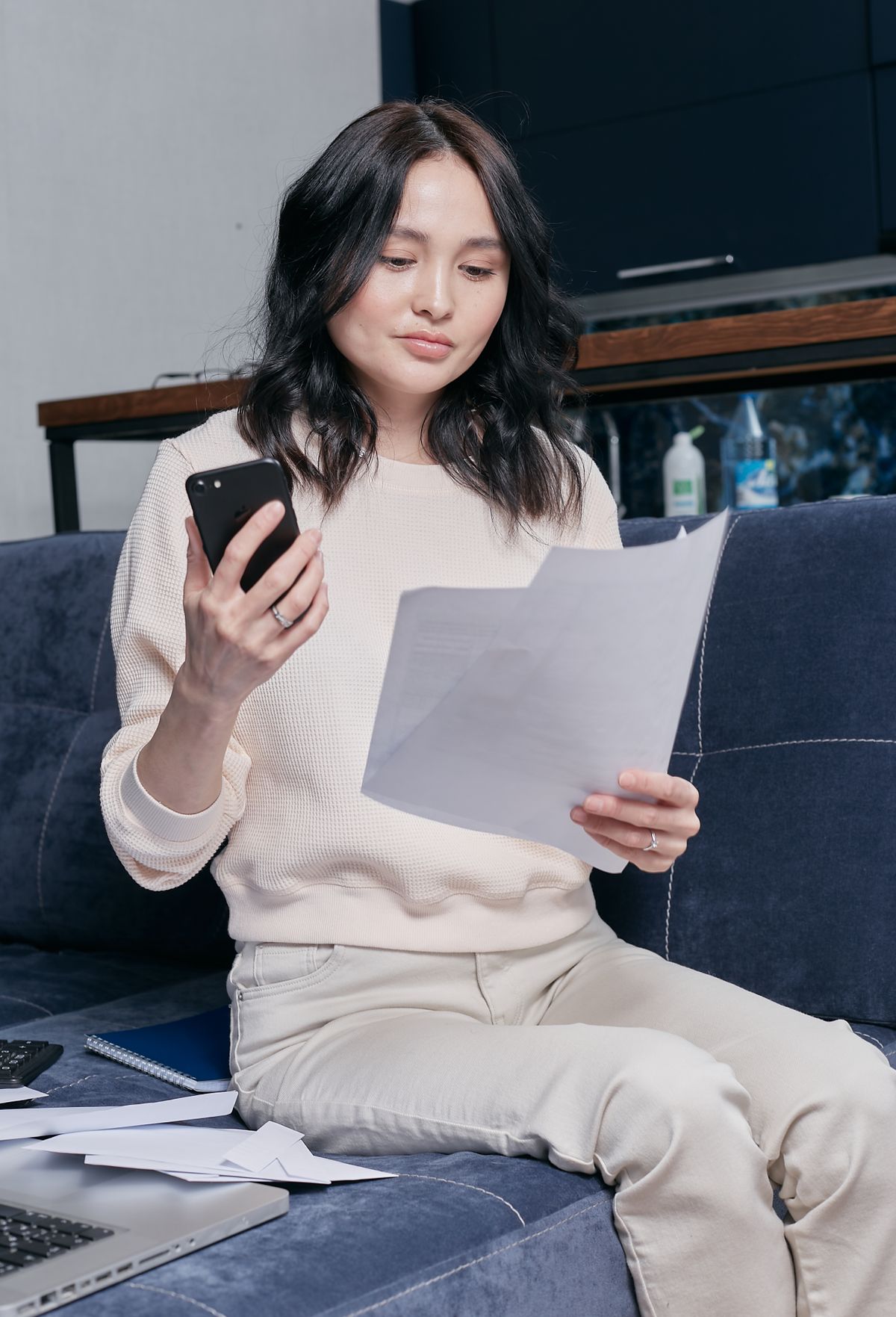 소파에 앉아 휴대폰과 서류로 가계 재정을 관리하는 여성