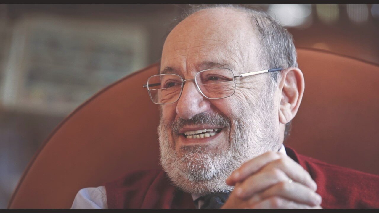 움베르토 에코가 서재의 의자에 앉아 웃고 있는 모습