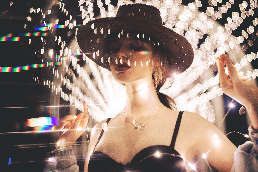 모자를-쓴-여성이-어둠-속-아련하게-흩어지는-조명-속에서-편안하게-포즈를-취하고-있다