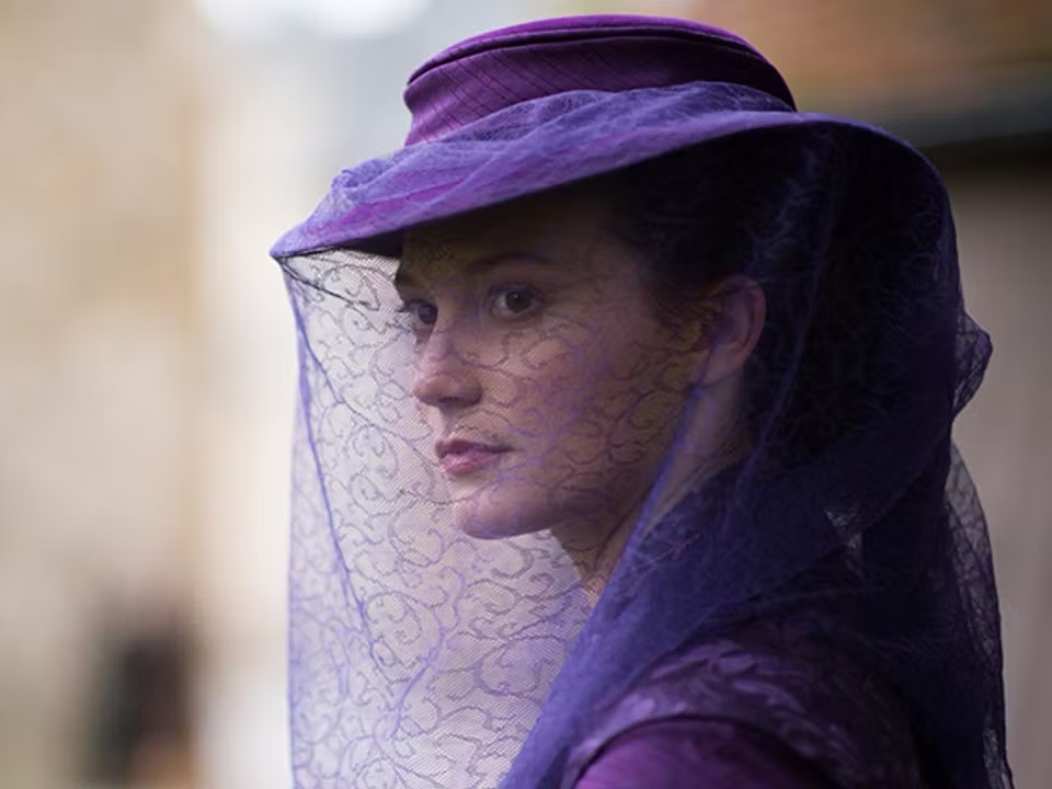 보라색 모자와 레이스 베일을 쓴 여성이 옆을 바라보고 있는 모습. 얼굴을 가볍게 가린 보라색 망사 베일과 우아한 클래식 의상이 인상적인 장면.