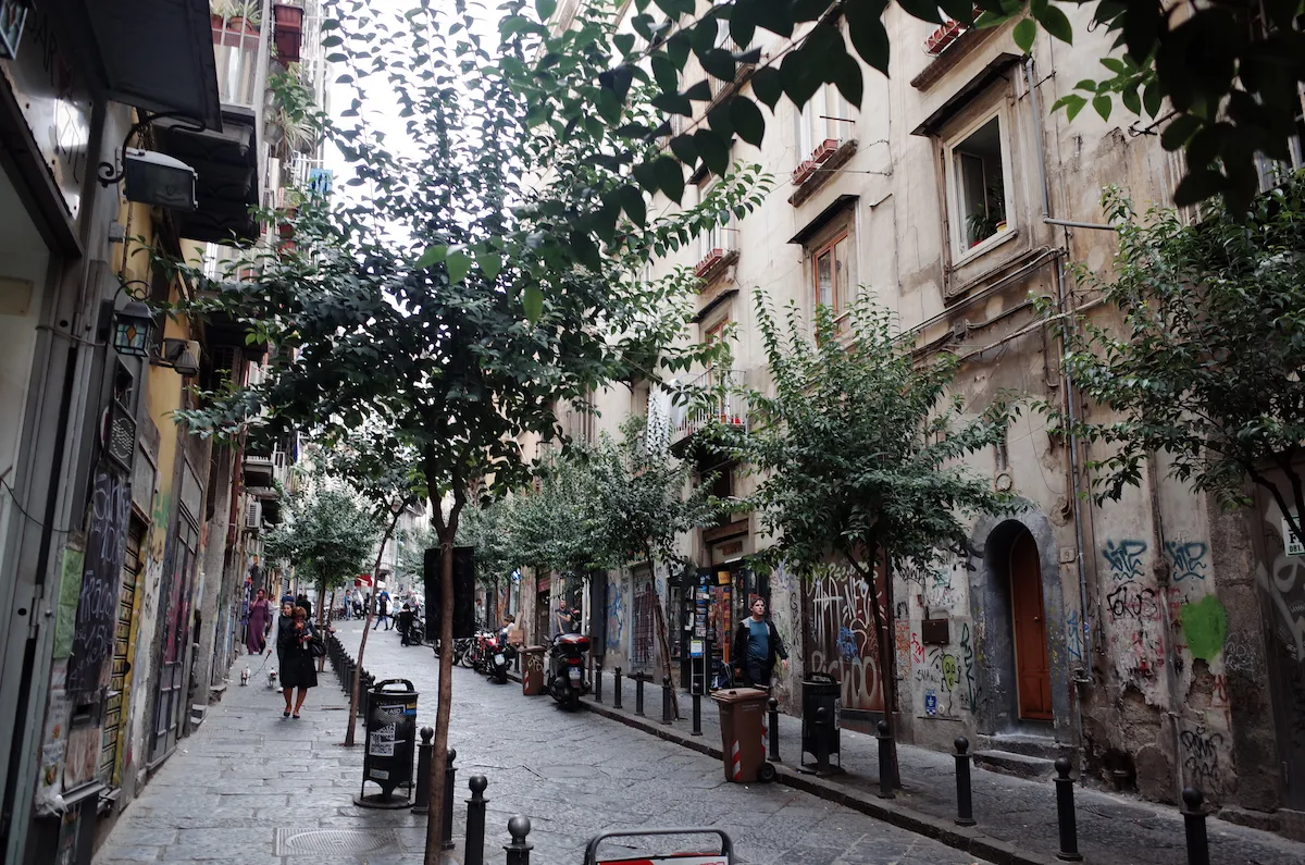 나무가 심어진 나폴리의 평화로운 보행자 전용 돌바닥 골목과 벽면에 그려진 그래피티들
