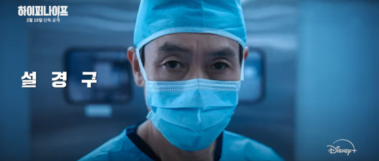 수술복과 마스크를 착용한 남성이 날카로운 눈빛을 보인다.