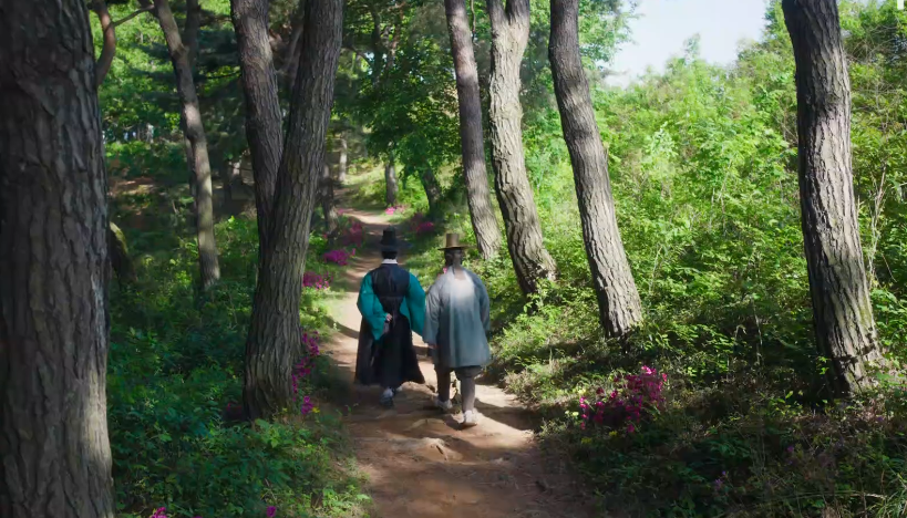 두 사내가 기다란 소나무 숲길을 따라 걷는 뒷모습이 보인다.