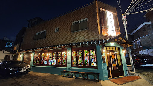 서울 혜화동의 커피한약방 혜화점 외관 야경. 붉은 벽돌 건물에 형형색색 스테인드글라스 창과 한약방 간판이 돋보이는 분위기 있는 카페.